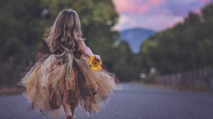 young girl in make believe dress running down the road