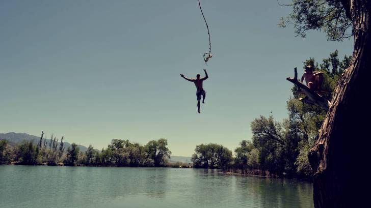 man swinging from a rope over a lake and letting go