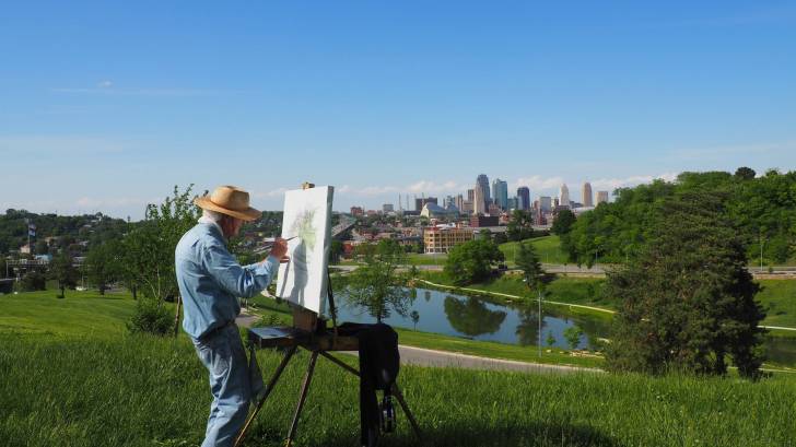 older man painting a scene on a sunny day