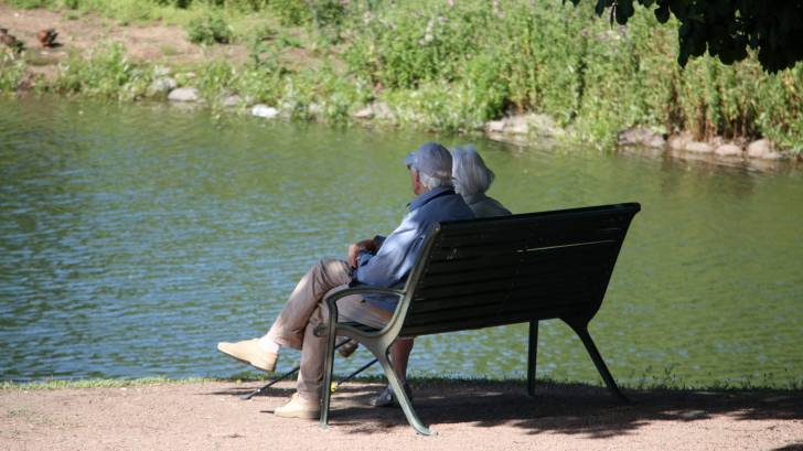 older people sitting on a bench by a lake