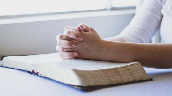 hands folded on a bible saying prayers