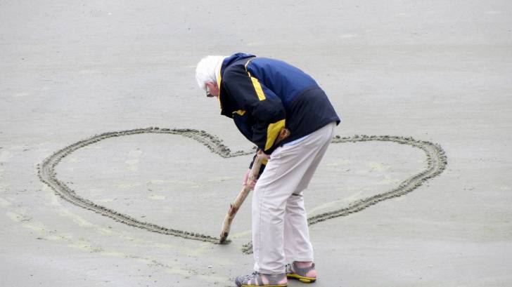 older man drawing a heart on beach