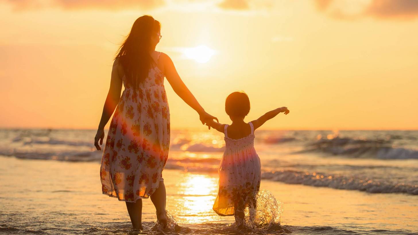 mom and young daughter walking on beach at sunset