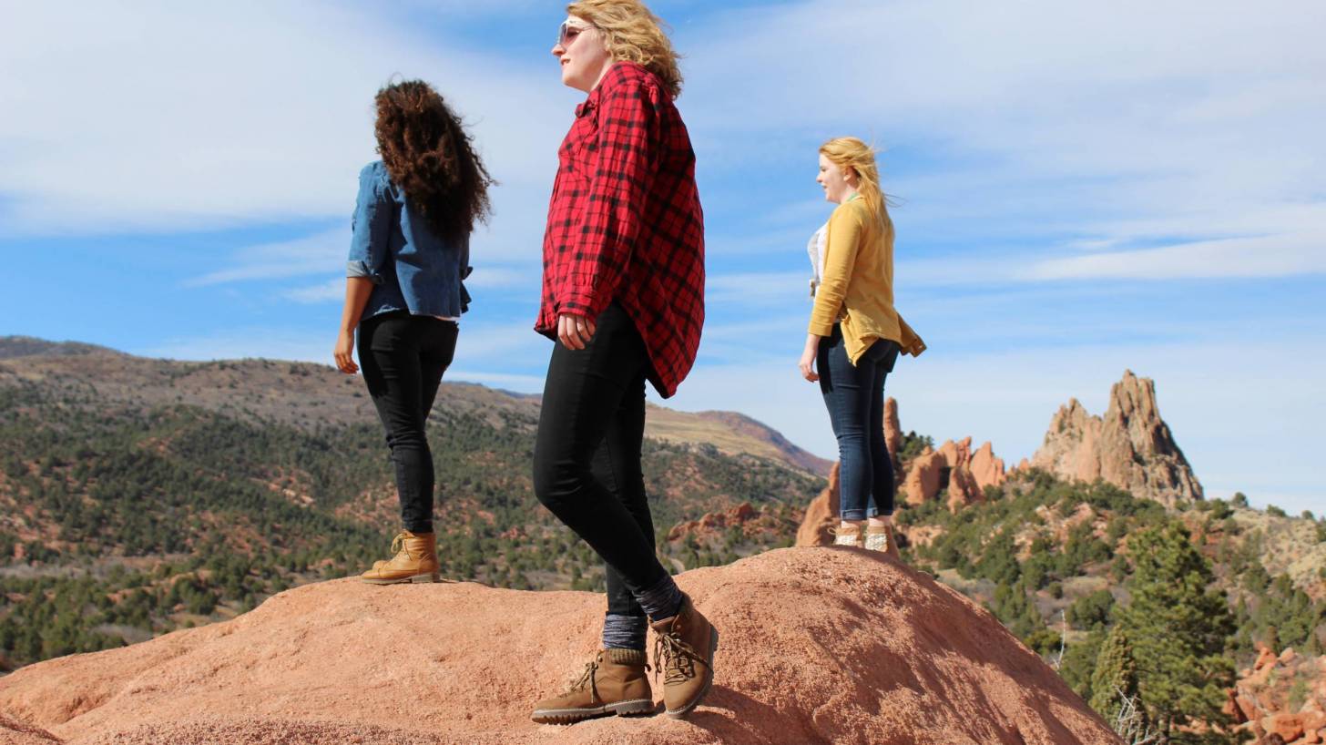 three young women on mountain top looking out at blue sky