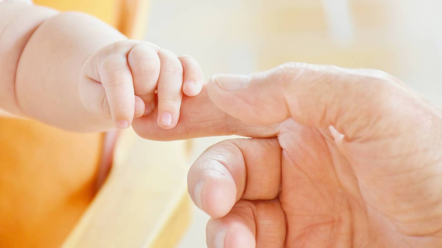 older hand touching a baby's hand