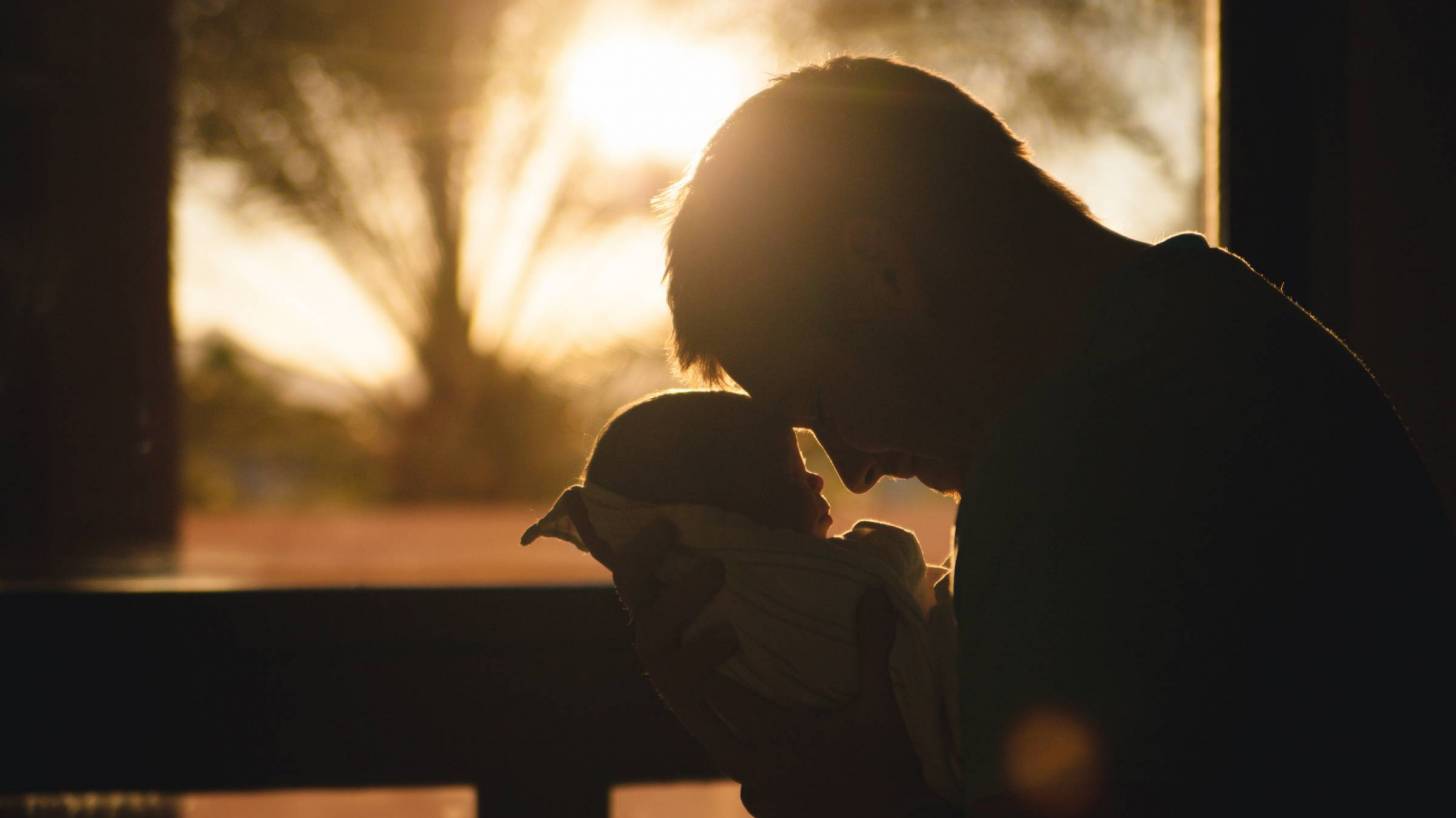 father holding new born infant with the sun setting in the background