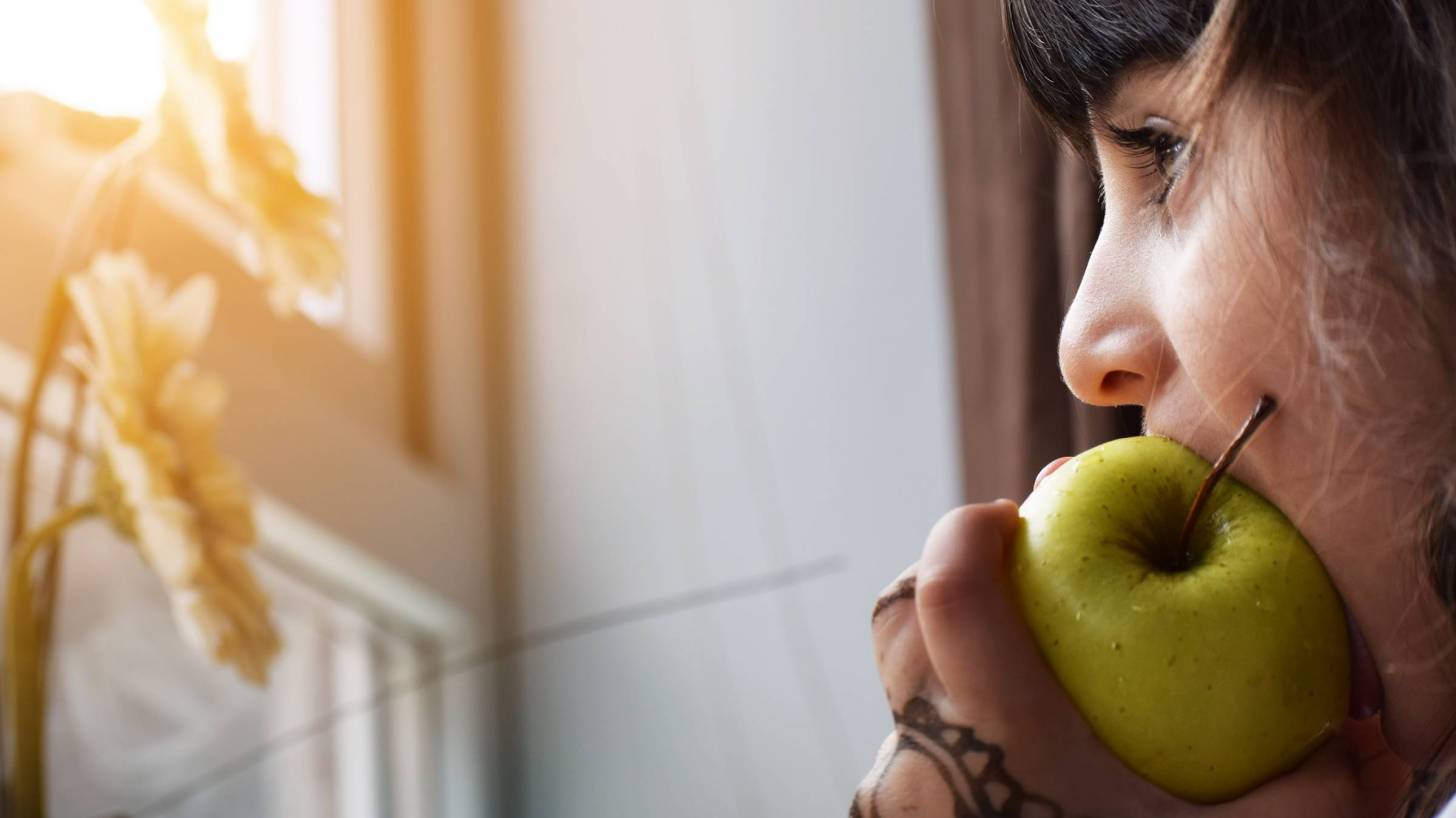 young girl eating a green apple looking out a window