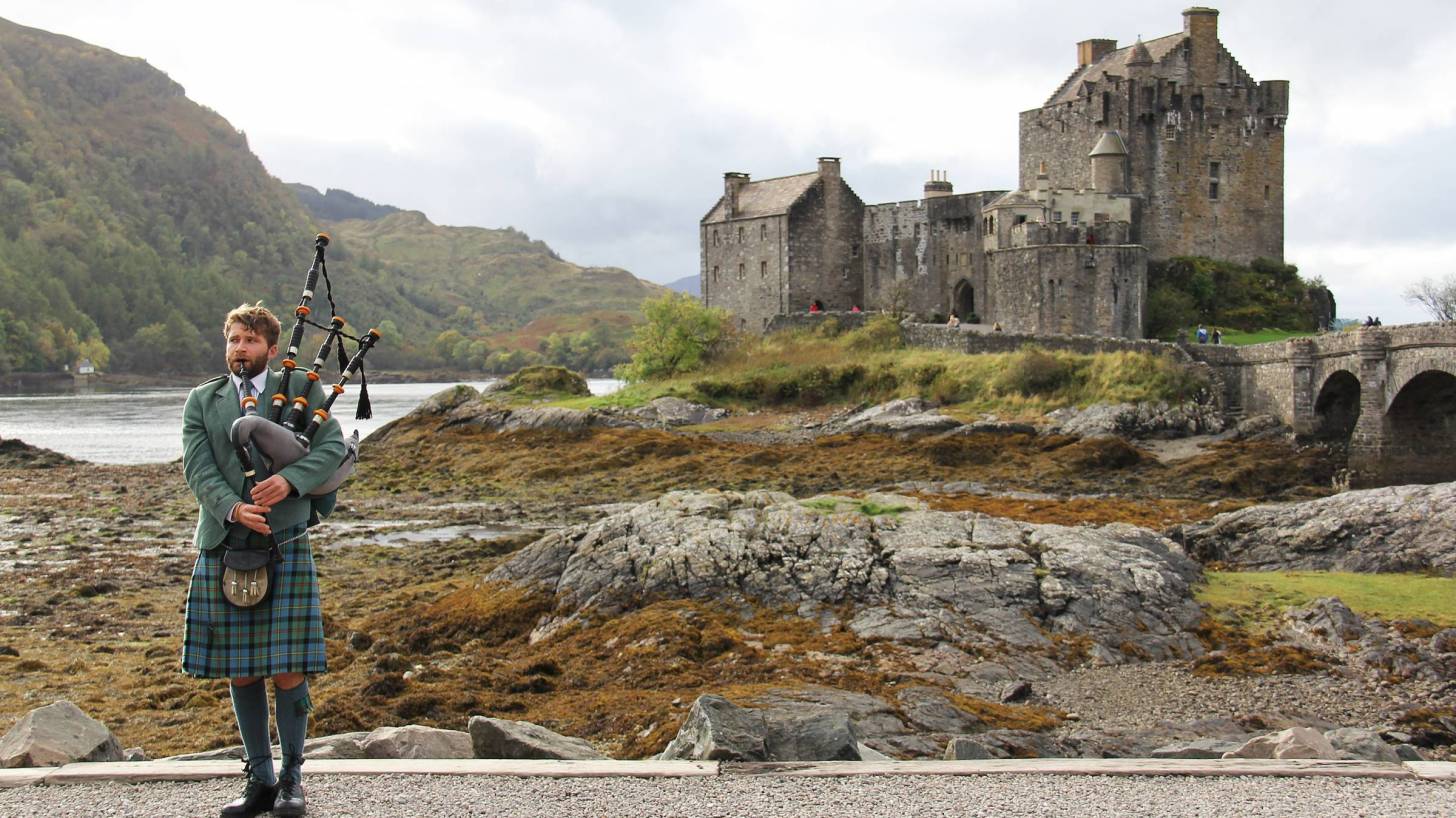 young man playing the bag pipes in the highlands
