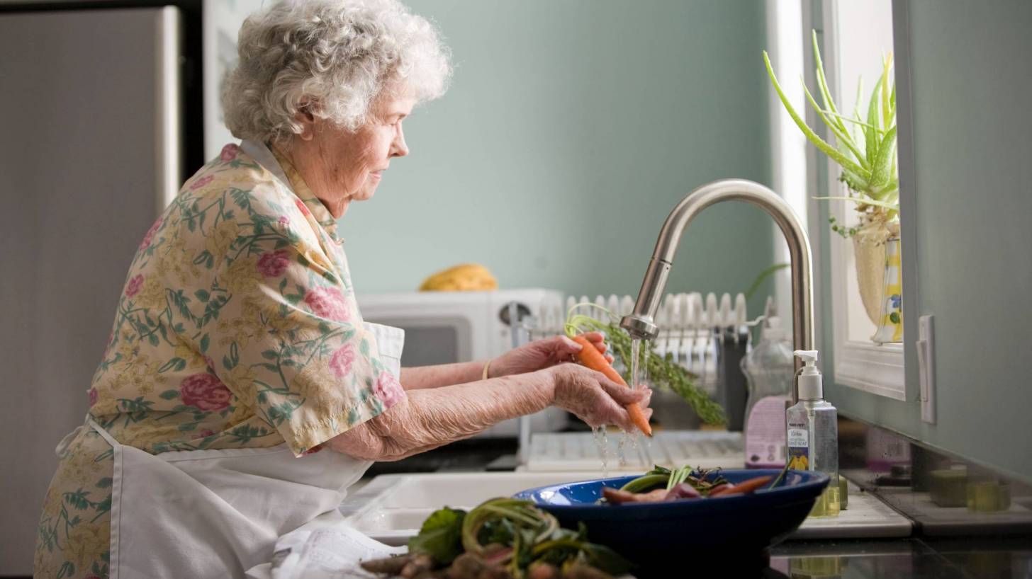 older woman in kitchen washing veggies
