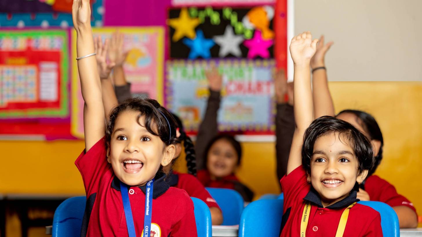 young children in school happy and raising hands