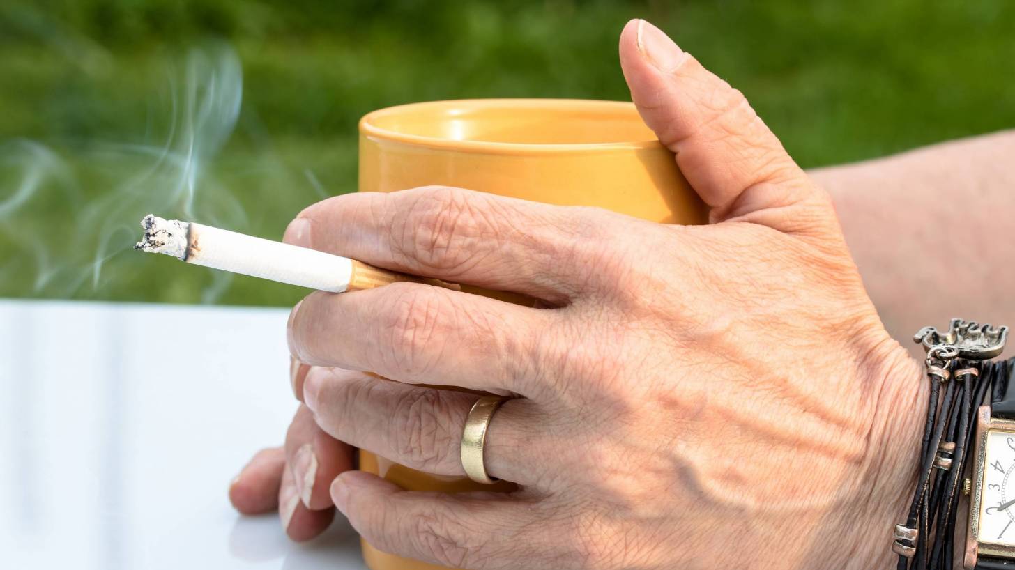 person smoking a cig with a cup of coffee