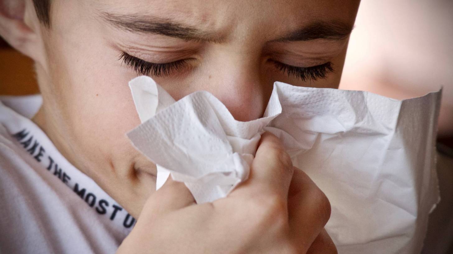 young boy sneezing into a tissue