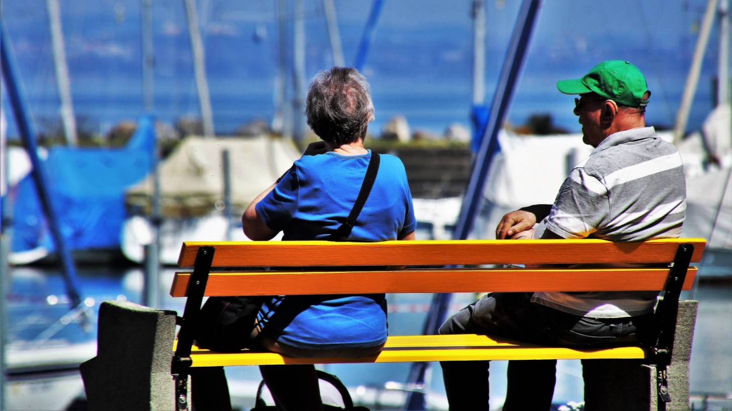 older cou-ple sitting on bench by a marina