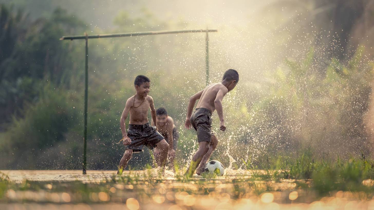 young boys playing soccer in muddy field
