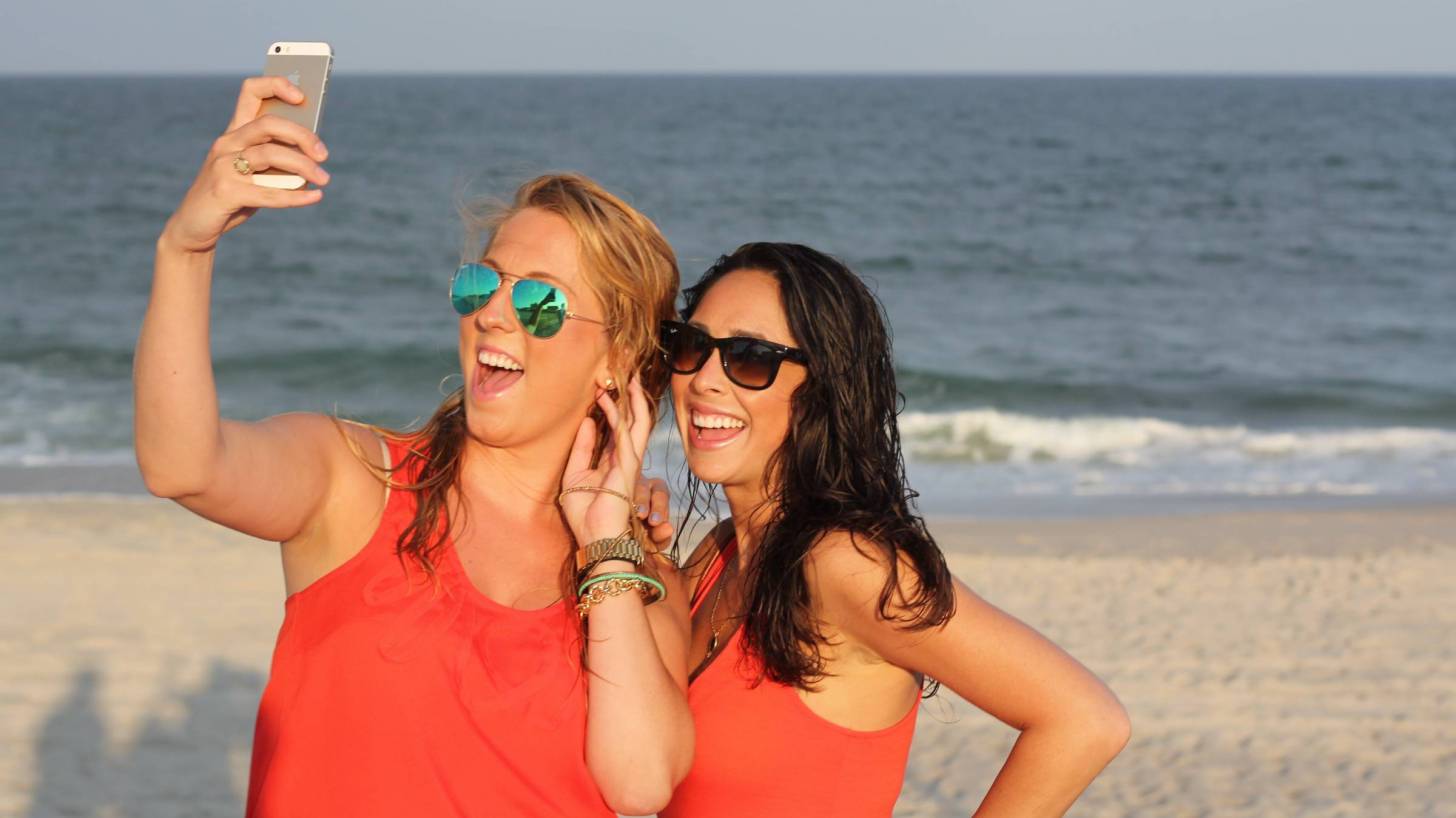young girls on beach smiling and taking selfie