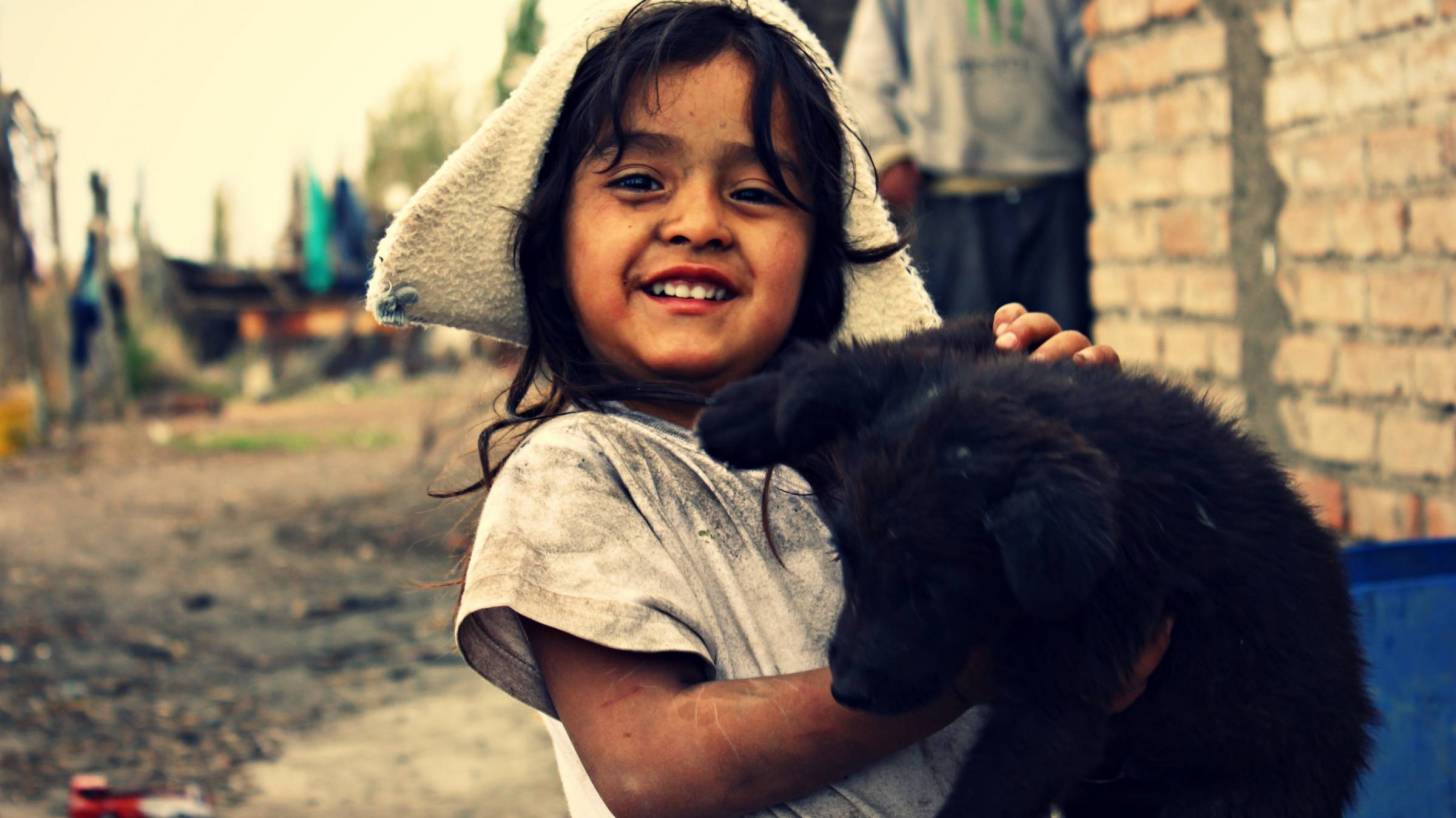 young girl in poverty holding black puppy, smiling