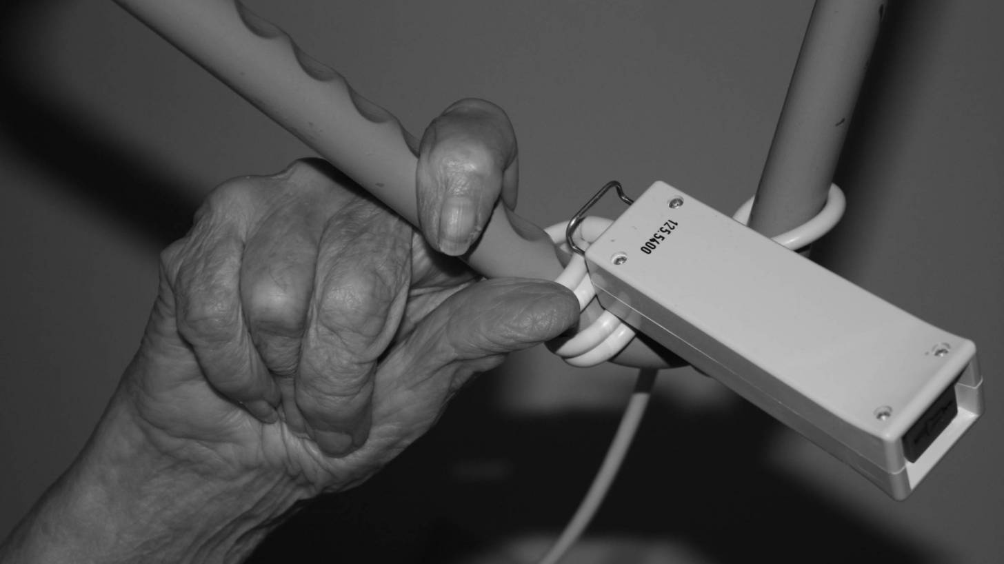 old person's hand holding on a hospital bed rail
