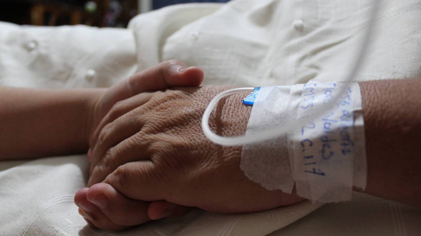 older hospital patient holding hand of a loved one