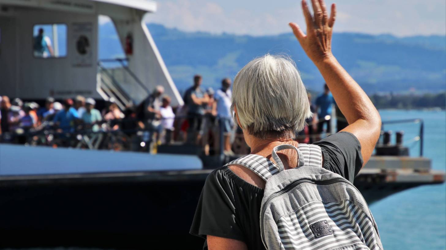 older woman waving to a ferry boat full of people