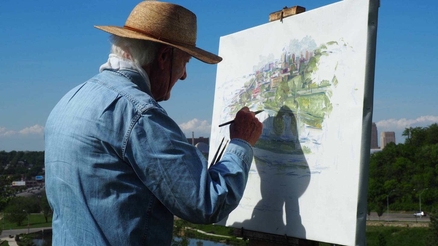 older man painting on a canvas outside