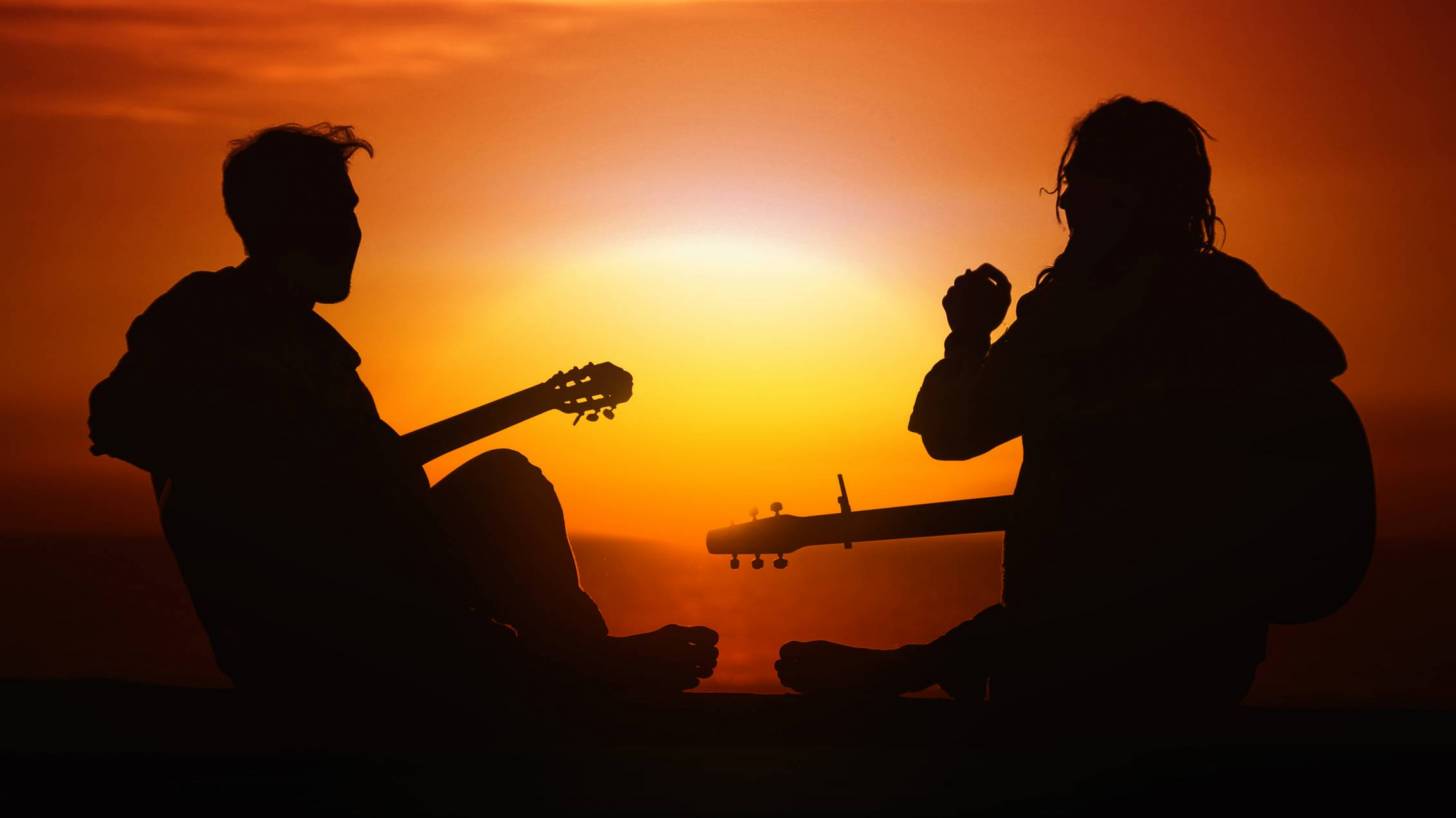 two people playing the guitar at sunset