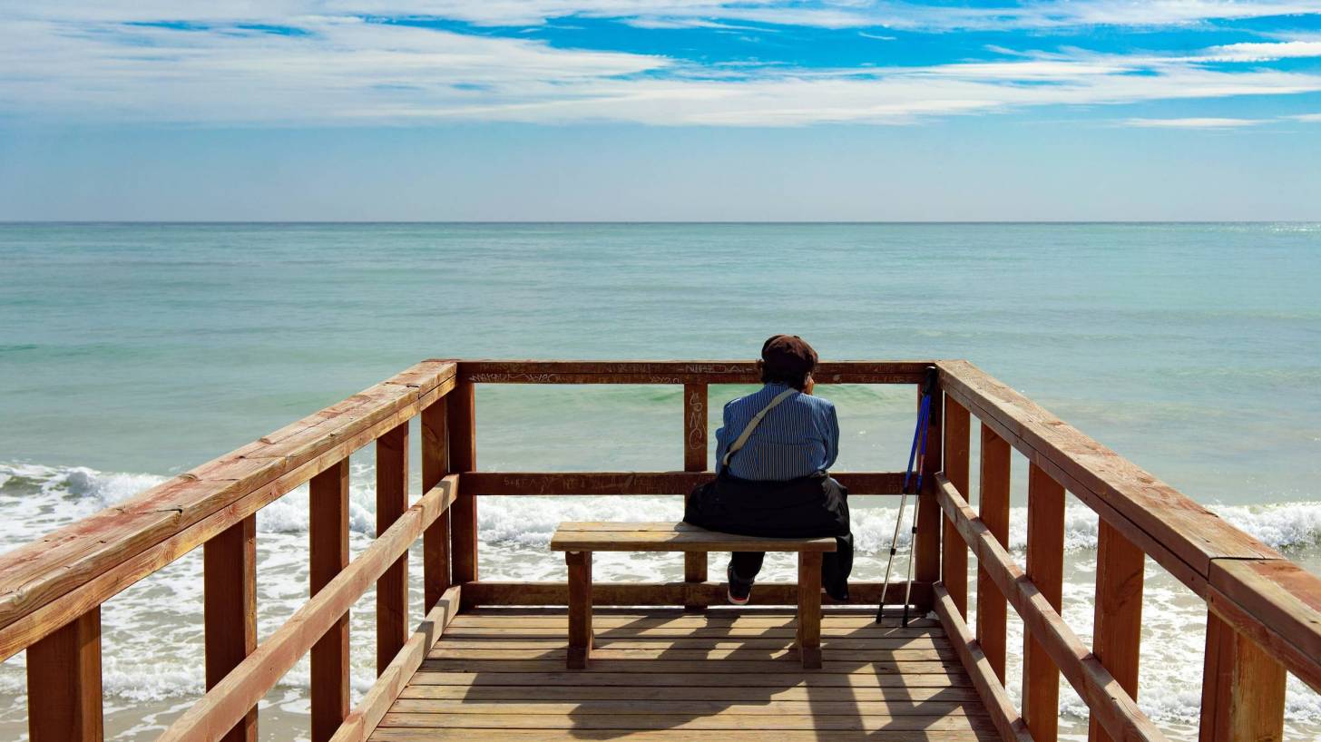 old man sitting on bench looking at the sea