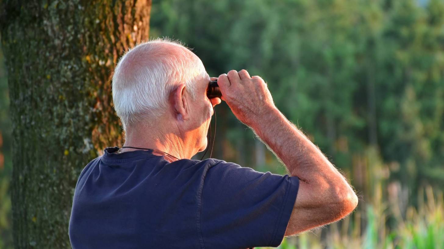 senior man with binoculars walking in the woods