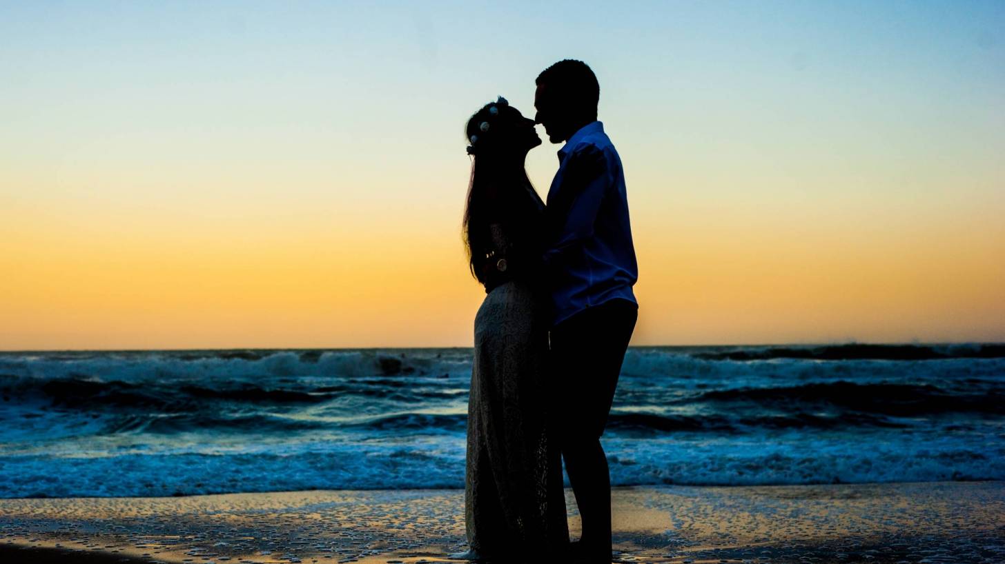 pregnant husband and wife on a beach at sunset in a silhouette