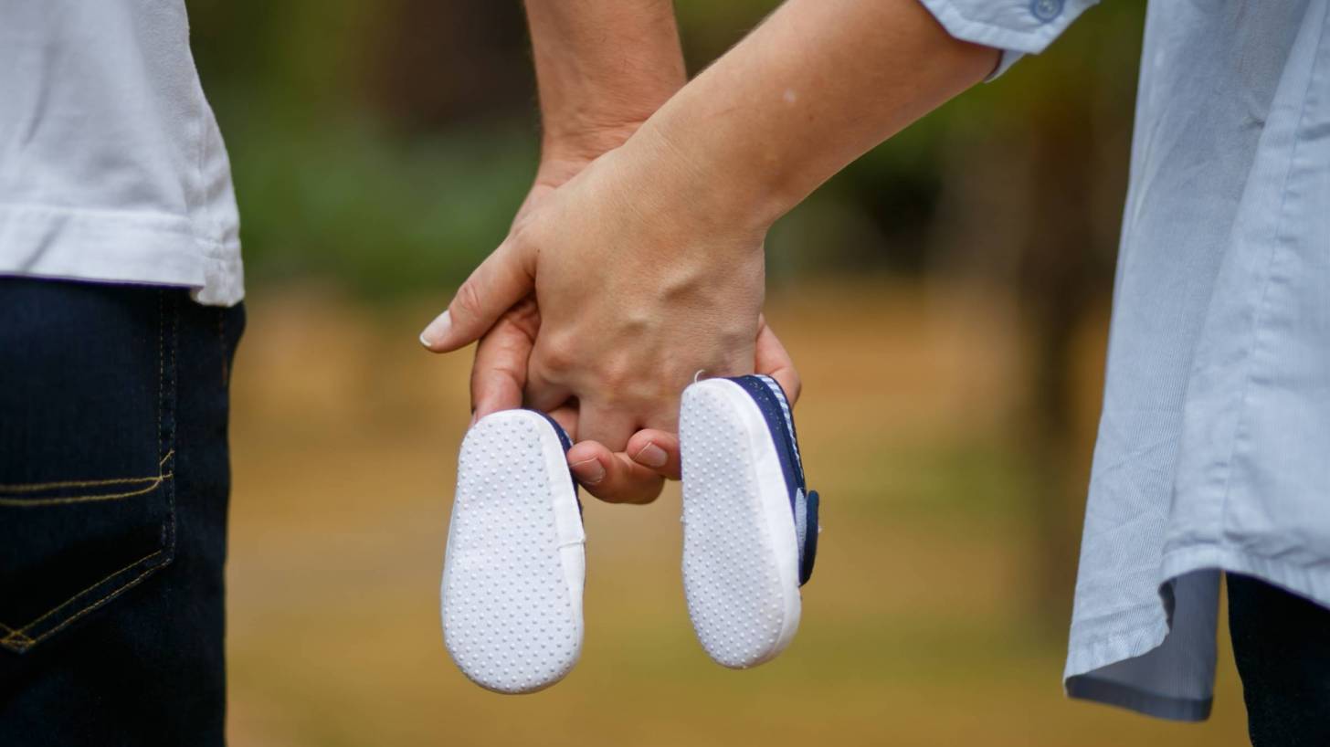 man and wife holding baby shoes