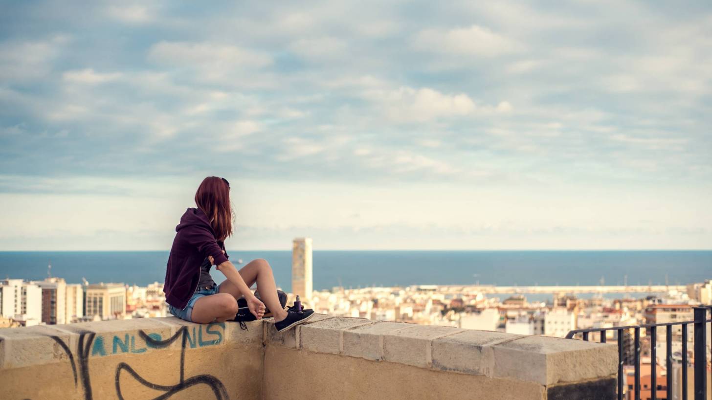 girl on a wall looking over a spanish city and to the ocean