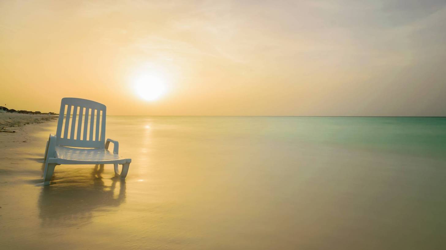 lone chair with sun setting over calm beach