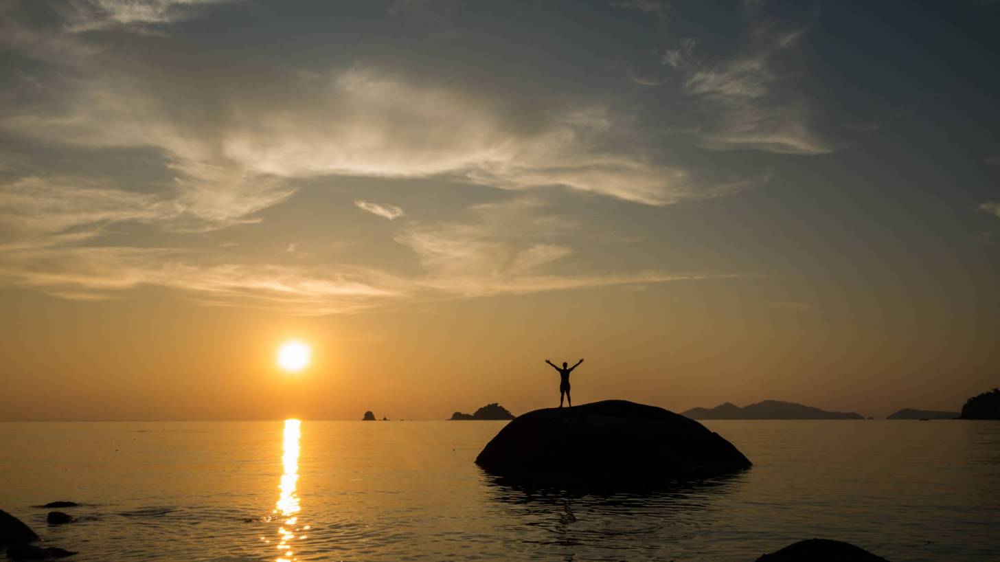 sun setting in the southern hemisphere, man celebrating on a rock