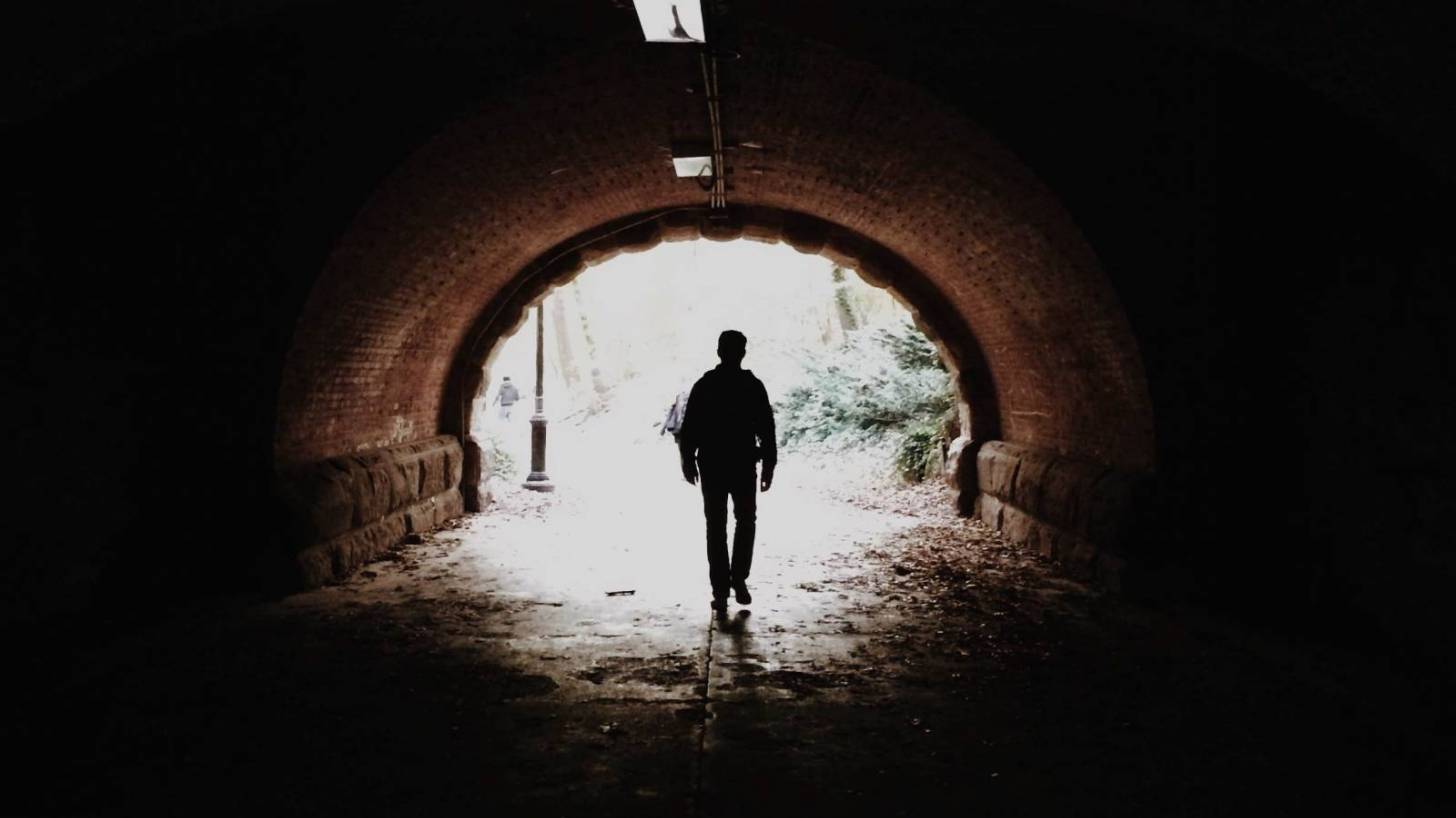 man walking in a tunnel heading towards the light, hopeful