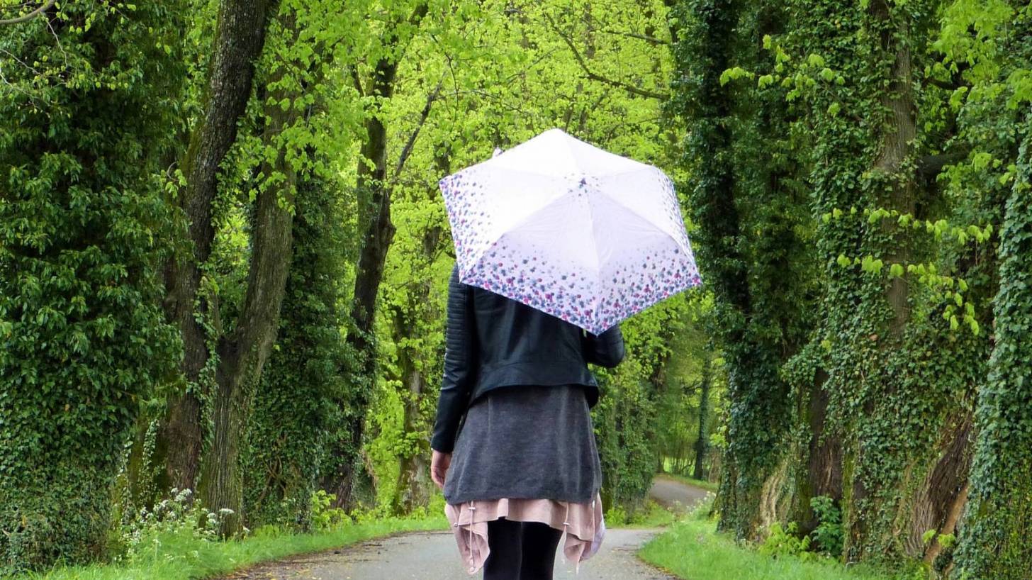 young women with an umbrella wlaking down a tree lined path
