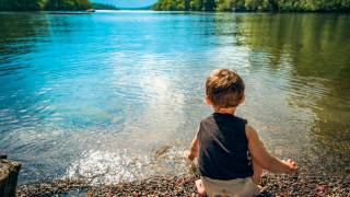 young boy sitting on the edge of a calm lake