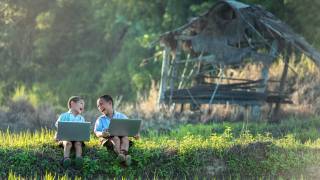 two children laughing working on their lap tops outside