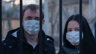 two people with masks on their faces looking through a fence