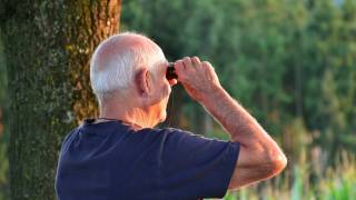 senior man with binoculars walking in the woods