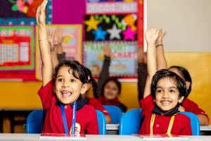 young children in school happy and raising hands